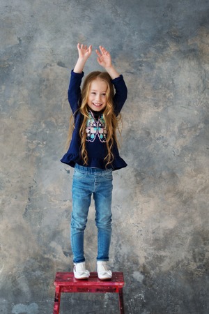 Cute Little girl standing on a red chair. Gray background.の写真素材