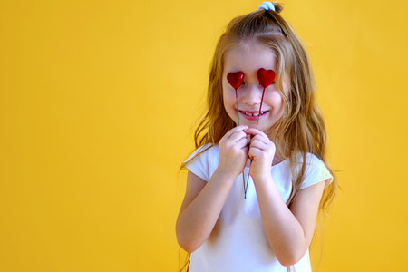 Little girl holding two little red hearts. The concept of Valentine's Day. Yellow background.の写真素材