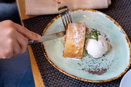 Apple strudel with vanilla ice cream and mint. The girl's hands are cut with a knife and fork.