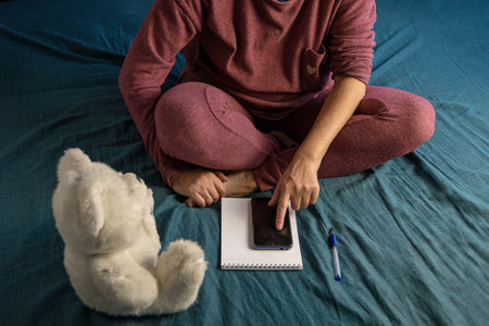Woman is sitting in a tracksuit on a bed at home. Plan your day in Notepad. Color of bed linen tidewater greenの写真素材