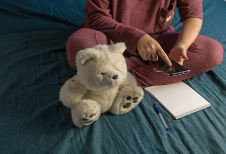 Woman is sitting in a tracksuit on a bed at home. Plan your day in Notepad. Color of bed linen...