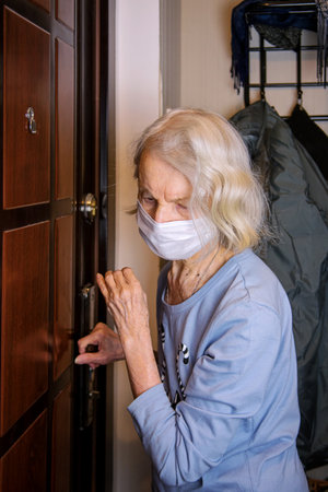Stay at home. Self-isolation to prevent the coronavirus pandemic. An older woman in a protective mask looks through the peephole. Covid-19 concept.の写真素材