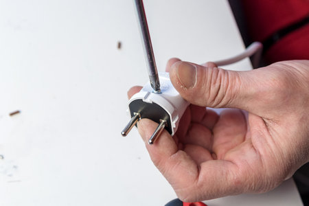 Close-up on the hands of a Caucasian electrician holding a screwdriver, working on the plug of an electrician on a white background. Collecting the socketの写真素材