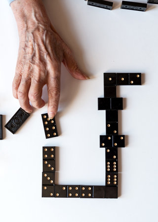 Family entertainment for a fun leisure game of dominoes. The hand of an elderly woman puts a domino on the table.の写真素材
