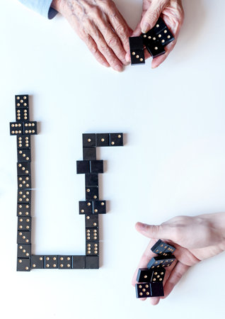 Family entertainment for a fun leisure game of dominoes. Grandson and grandmother play dominoes. The view from the top.の写真素材
