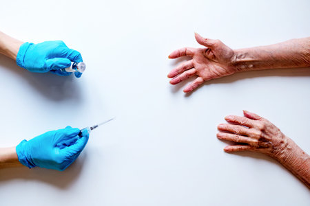 Medical syringe and ampoule with medicine in the hands of a doctor in medical gloves on a white background, the outstretched hands of an elderly woman. Serum or vaccine in a syringe with a needle. copy the space. flatleyの写真素材