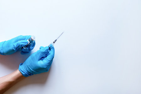 Medical syringe and ampoule with medicine in the hands of a doctor in medical gloves on a white background. Serum or vaccine in a syringe with a needle. copy the space. flatleyの写真素材