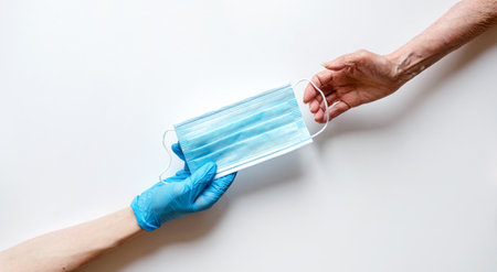 The doctor's hands in medical gloves on a white background pass the mask to an elderly woman