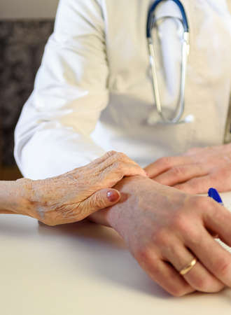 An elderly patient placed her hand on the arm of a geriatric doctor at the clinic.