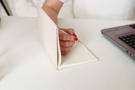 Close-up of a young woman's hands writing a plan of the day in a notebook at the workplace at the...