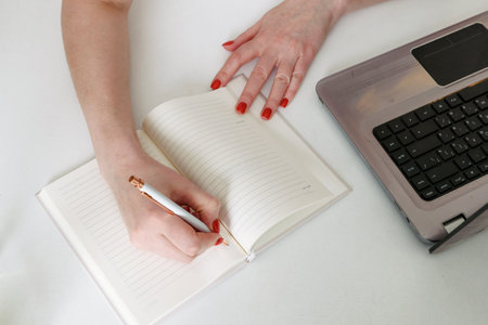 Close-up of a young woman's hands writing a plan of the day in a notebook at the workplace at the computer. The concept of working and studying at home.の写真素材