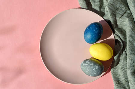 Pink ceramic plate with colorful Easter eggs in pastel colors on a pink background. Happy Easter card concept, minimalistic design, top view. Natural paintの写真素材