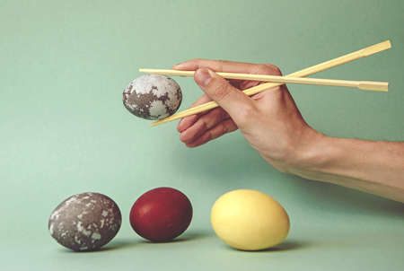 A space egg in the hands of a young man with Japanese chopsticks on a neon background. Minimal...
