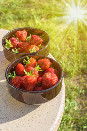 Fresh strawberries, illuminated by sunlight, in black plates on a granite table.の写真素材