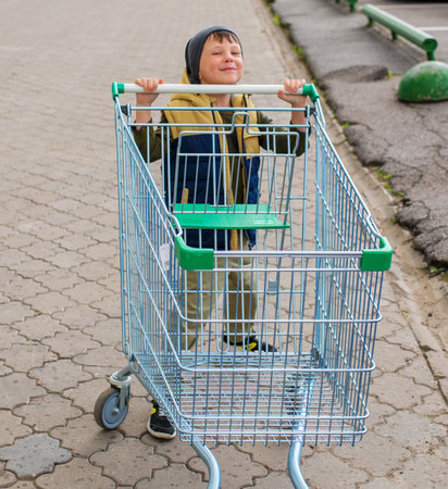 Kid boy pushing empty shopping cart at parking lotの写真素材