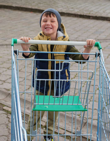 Kid boy pushing empty shopping cart at parking lot.の写真素材