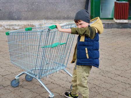 Kid boy pushing empty shopping cart at parking lot.の写真素材