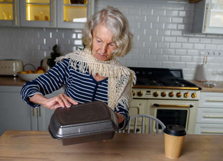 Lonely elderly woman opens food delivery from an online storeの写真素材