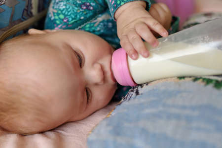 Three month old girl drinks milk from a bottleの写真素材