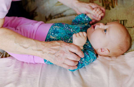 Hands of an elderly grandmother hold the hands of a three month old girl.の写真素材