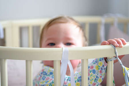 Cute girl of ten months old, playing alone in a crib at home in the afternoon or in the morning.の写真素材