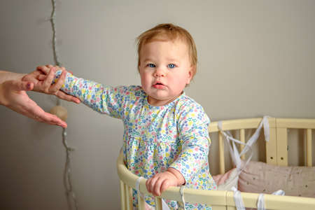 Cute girl of ten months old, playing alone in a crib at home in the afternoon or in the morning.