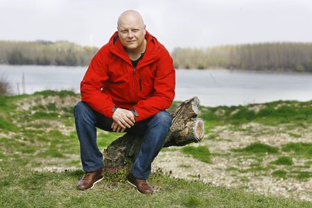 A man in a red jacket sitting on the tree in natureの写真素材