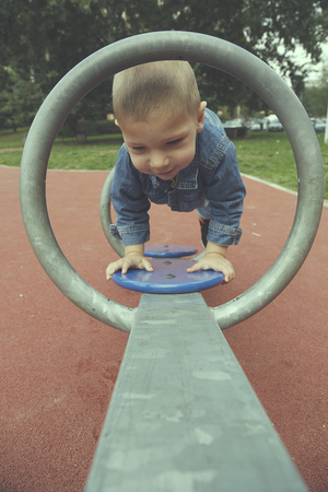 Happy child boy playing seesawing in green grass playground in parkの写真素材