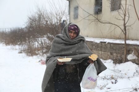 Belgrade, Serbia - January 10, 2017: A migrant eats free food during a snowfall outside a derelict customs warehouse. Migrant mostly from Afghanistan and Pakistan, have occupied an abandoned customs warehouse in Belgrade as they seek ways to move on towarのeditorial素材