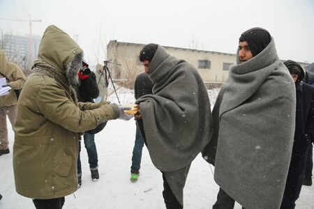 Belgrade, Serbia - January 10, 2017: A migrant eats free food during a snowfall outside a derelict customs warehouse. Migrant mostly from Afghanistan and Pakistan, have occupied an abandoned customs warehouse in Belgrade as they seek ways to move on towarのeditorial素材