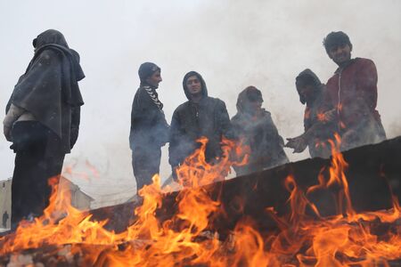 Belgrade, Serbia - January 10, 2017: Migrants warm themselves by the fire in front of an abandoned...