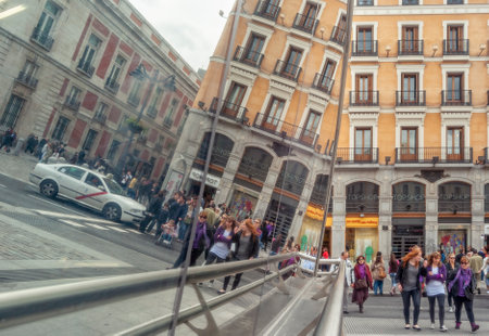 Street scene in Madrid's Puerta del Sol, with reflections of its metro station made of glass. Three girls walk and are reflected in the glass, along with more peopleのeditorial素材