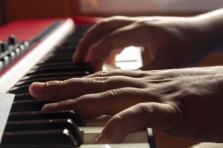 Hands playing a musical keyboard. First hand in focus and the rest of the image out of focusの写真素材