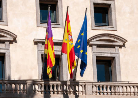 Flags of Europe, Spain and Balearic Islands on three masts on the facade of a public buildingの写真素材
