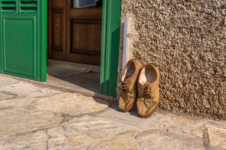 Rustic brown shoes resting on the wall of the facade of a rural house of green blindsの写真素材