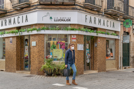 Llucmajor, Spain; decemeber 17 2020: front of a pharmacy with a person walking down the street wearing a face mask. New normalのeditorial素材