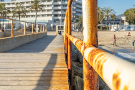 Close-up of a rusty metal railing in the harbor of Magaluf beach, island of Mallorca. In the background out of focus, the beach with families enjoying the good weatherの写真素材