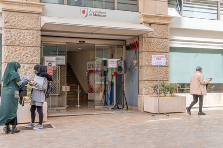 Manacor, Spain; March 18 2021: Main entrance of the Manacor City Hall with people waiting their turn outside and wearing face masks because of the Coronavirus pandemic. New normal conceptのeditorial素材