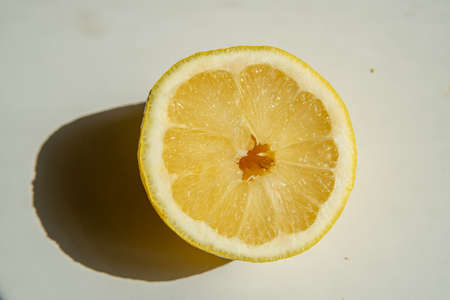 Close-up of a halved lemon in direct sunlight casting a strong shadow on a neutral background