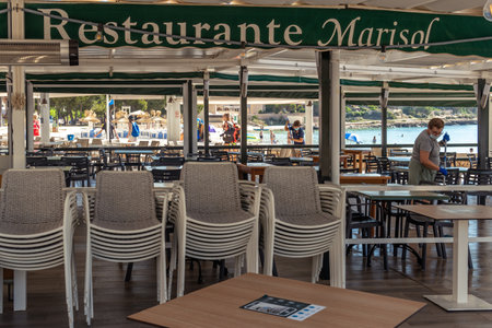 Colonia de Sant Jordi, Spain; July 02 2021: Restaurant terrace on the island of Mallorca with a woman cleaning with a face mask and nitrile gloves. Image of the new normal post Coronavirus pandemicのeditorial素材