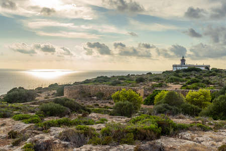 Cap Blanc lighthouse on the rocky coast of the island of Mallorca. In the background s seascape of the Mediterranean Sea at sunset with clouds. Sublime landscapeの写真素材