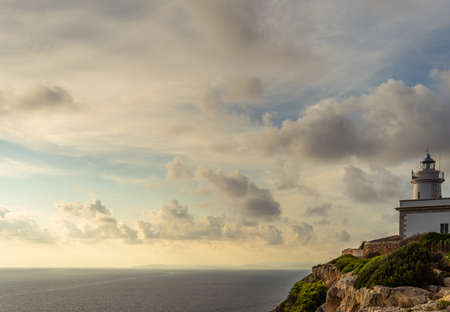 Cap Blanc lighthouse on the rocky coast of the island of Mallorca. In the background s seascape of the Mediterranean Sea at sunset with clouds. Sublime landscapeの写真素材