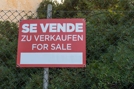 Red for sale sign, in Spanish, German and English language, on a metal grilleの写真素材