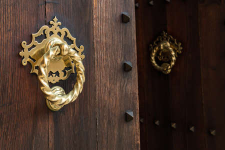 Close-up of a gilded metal knob on an open rustic wooden doorの写真素材