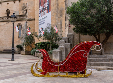 Manacor, Spain; december 01 2022: Red sled in a central square, with people walking around, in the Majorcan town of Manacor, Spainのeditorial素材