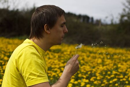 Young man blowing dandelion in the earlier april.の写真素材