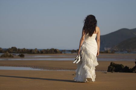 Bride walking in the beach with shoes in hand.の写真素材