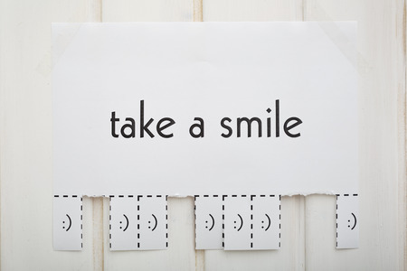 A paper with the phrase: Take a Smile and with a smile sign ready to be tore off. The photo is front.の写真素材