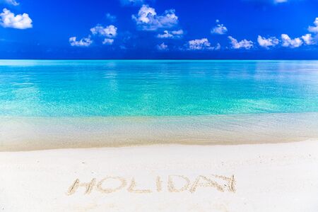 Word holiday written on sand in Maldives with the lagoon at background.の写真素材