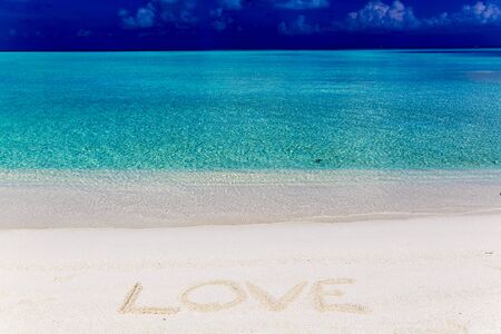 Word love written on sand in Maldives with the lagoon at background.の写真素材